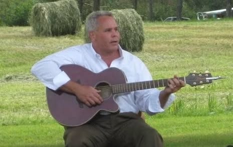 Eric playing acoustic guitar in a hayfield